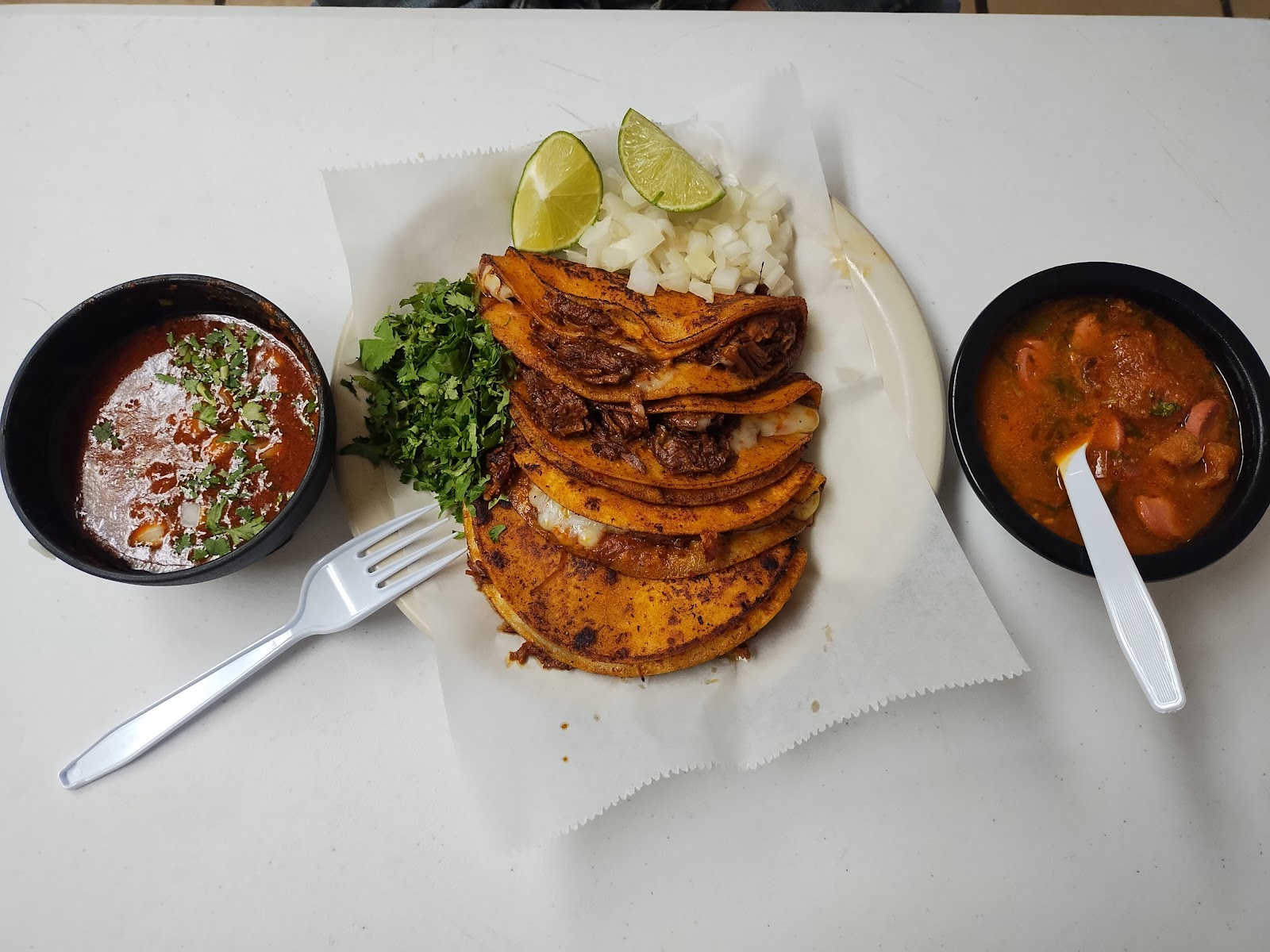 Stack of crispy birria tacos with consomé, cilantro, onion and lime